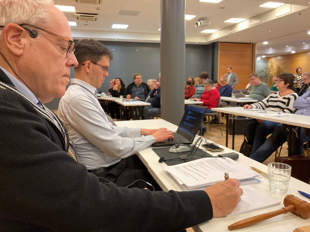 Två herrar vid podiet och i bakgrunden en stor sal med åhörare.